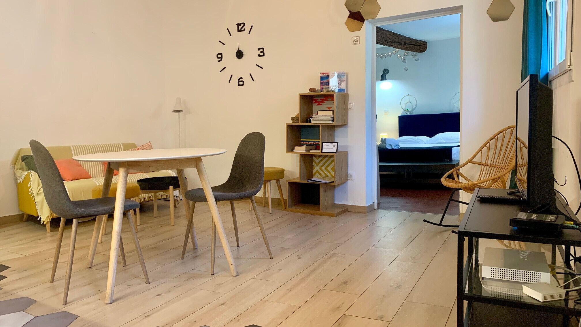 A compact living space with a dining table, two chairs, a sofa, a bookshelf, a bed, and a TV.