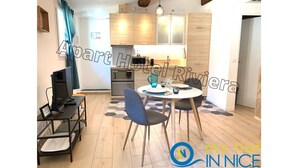 A modern kitchen with wooden cabinets, a dining area with a round table and chairs, and a small TV on a stand.