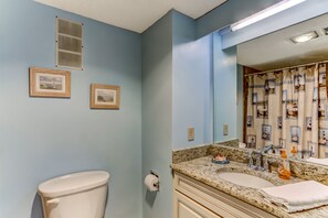 Une salle de bain avec des toilettes, deux tableaux encadrés au mur, un lavabo avec un miroir et un rideau de douche sur le thème de la marine.