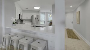 Una cocina moderna con armarios blancos, un lavamanos de acero inoxidable y una isla central con taburetes de bar.