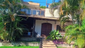 A residential house with a tiled roof, a wooden door, and a concrete pathway leading to the entrance. - Penthouse with pool, barbecue, and bathtub: Jeanne's Country House (Rio de Janeiro)