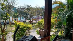 An outdoor exercise area with a stationary bike, a wooden bench, and a view of a playground and parked cars. - Penthouse with pool, barbecue, and bathtub: Jeanne's Country House (Rio de Janeiro)