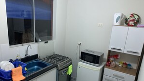 Una cocina compacta con estufa a gas, pileta, microondas y un refrigerador pequeño.