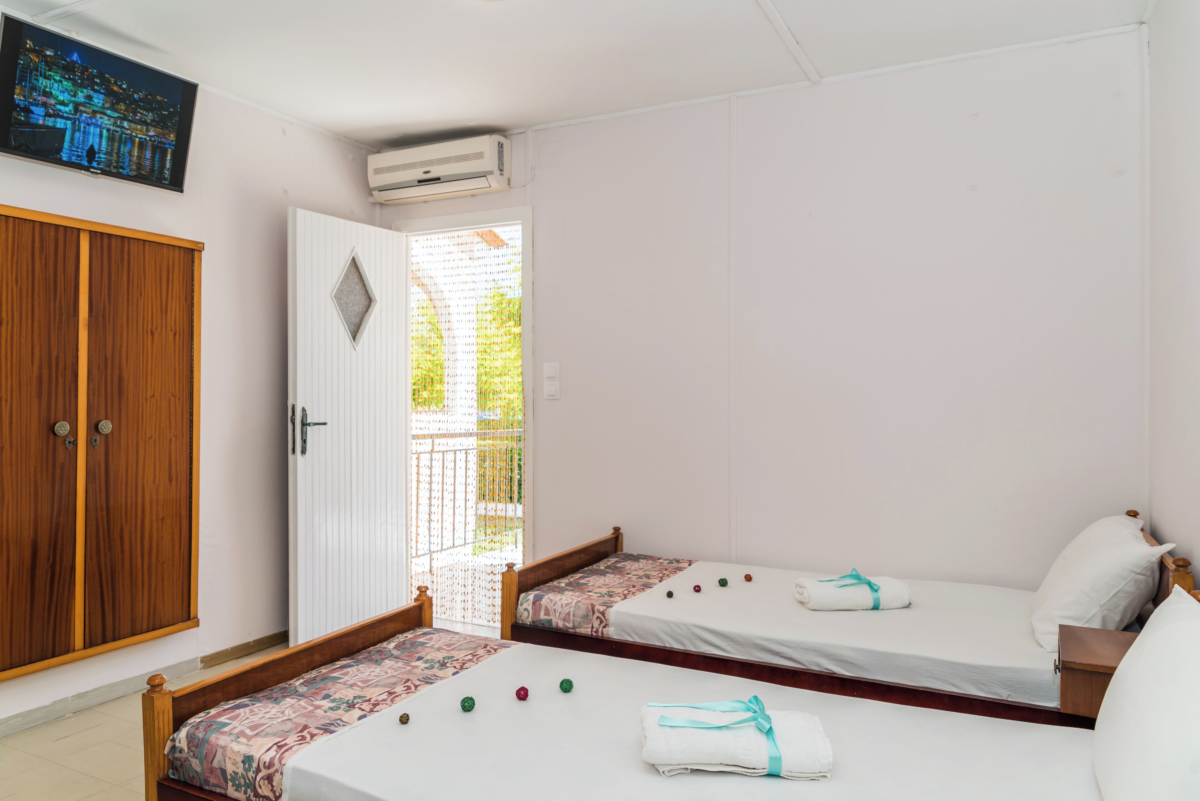 Habitación de hotel con dos camas individuales, un armario de madera, un televisor y un balcón con vistas.
