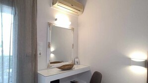 Un dormitori petit i funcional amb una tassa de mà, un mirall, una cadira, una taula de nit i un aparell d'aire condicionat.