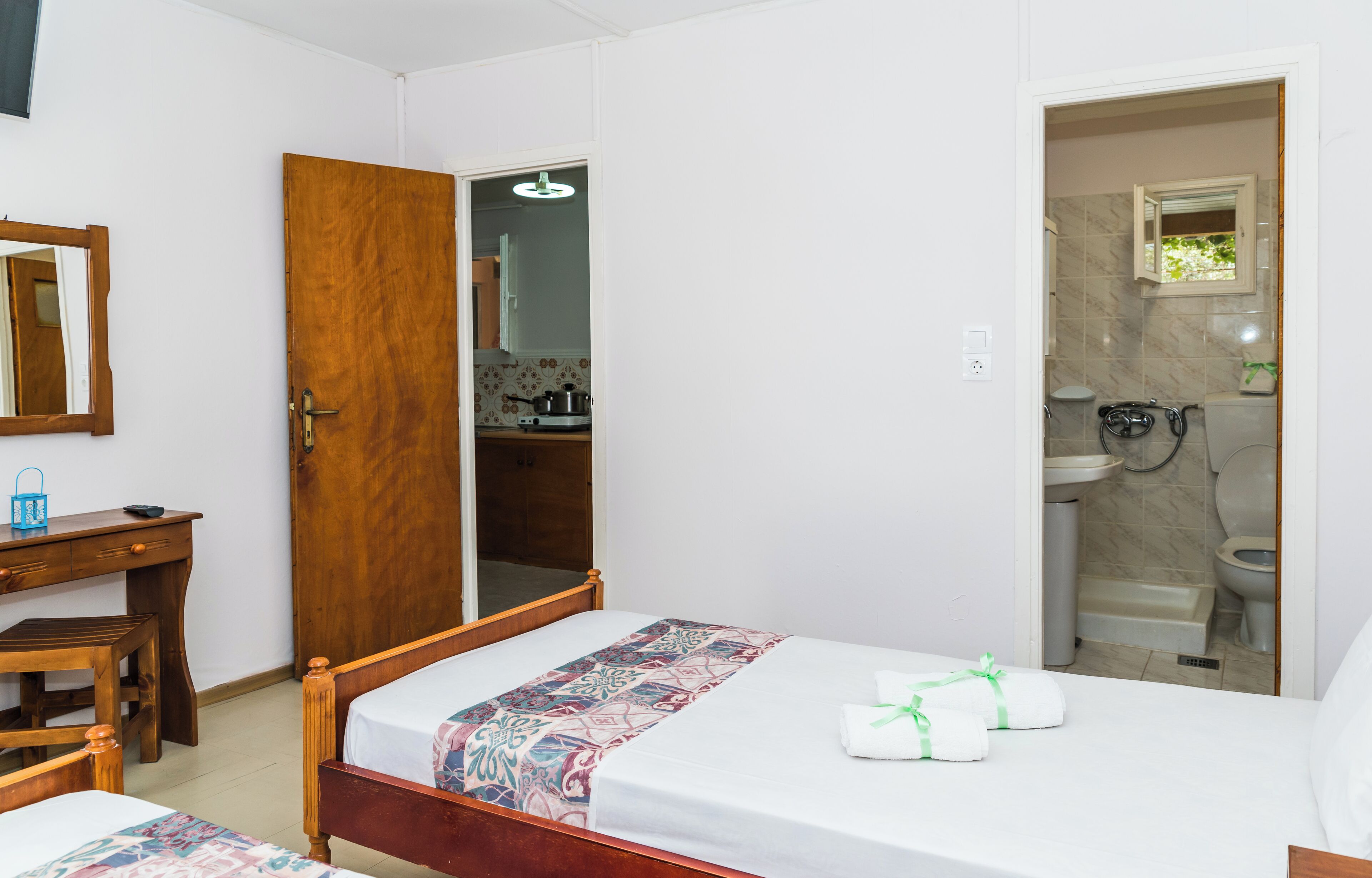 Un dormitorio con cama de madera, un escritorio y un baño visible a través de una puerta abierta.