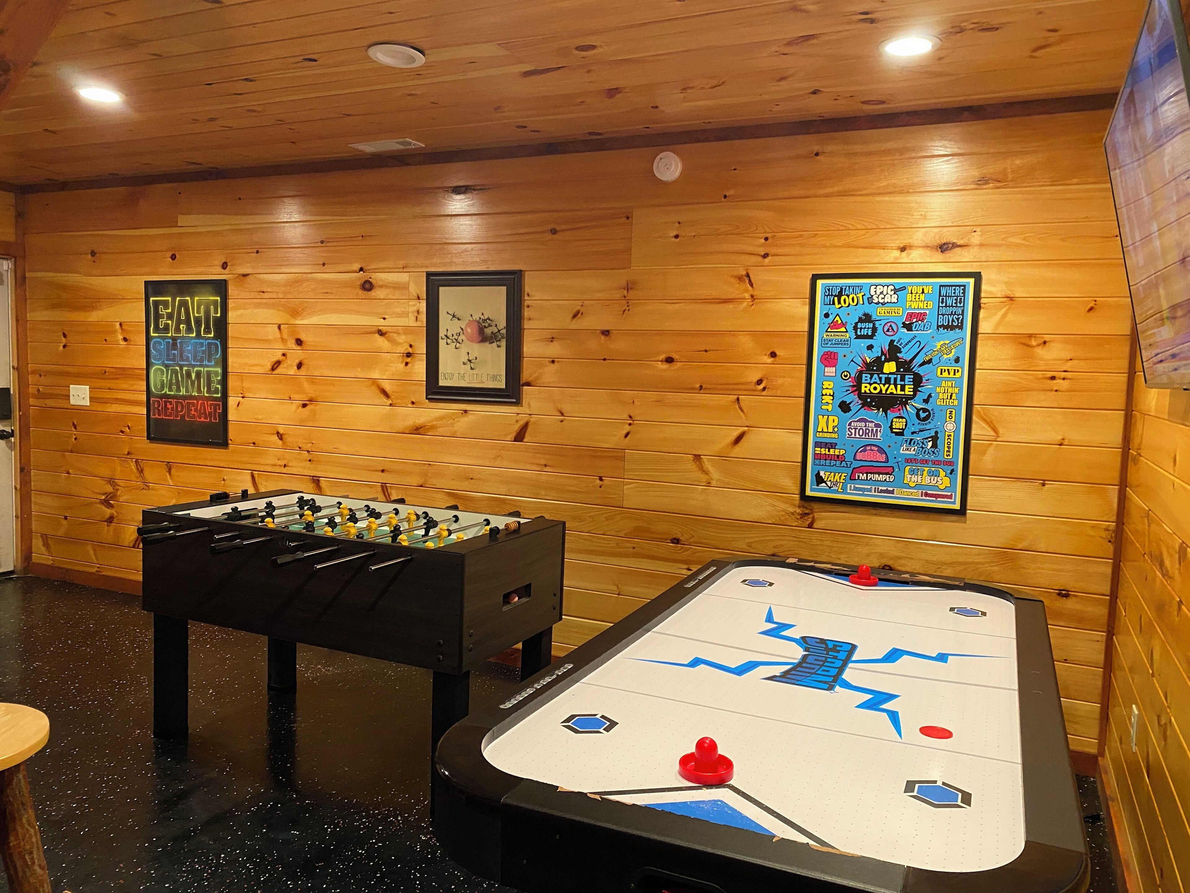 A room with wooden walls, a foosball table, and a shuffleboard table.