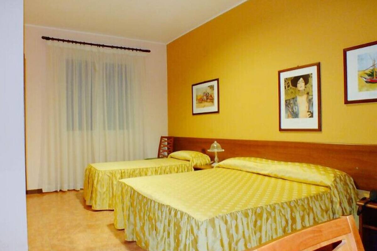 Ein Hotelzimmer mit zwei Betten, einem Holz-Kopfteil, einem Fenster mit Vorhängen und gerahmten Bildern an der Wand.