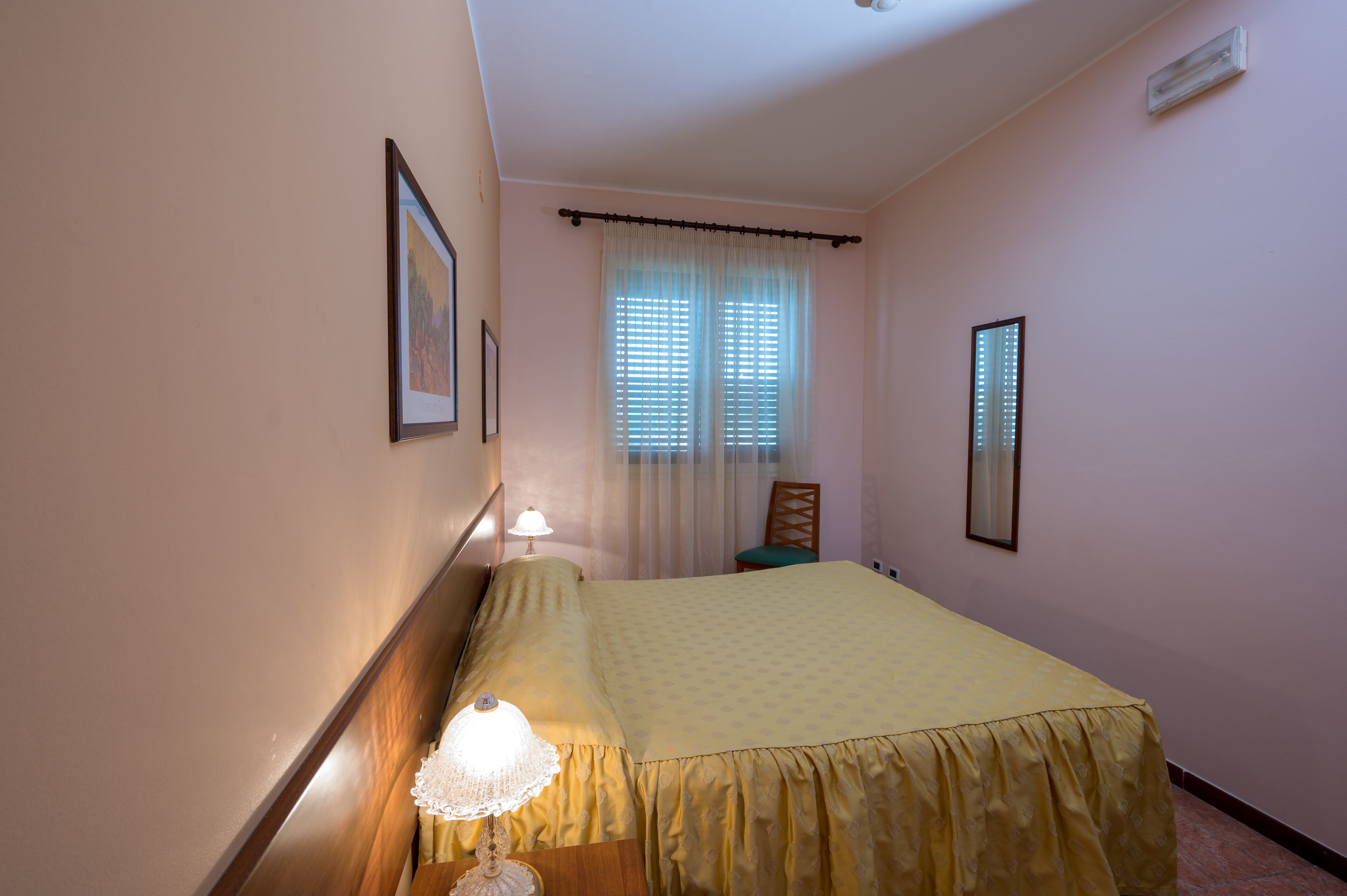Una camera da letto con un letto, un comodino con una lampada, una sedia e una finestra con tende.