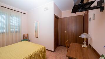 A bedroom with a bed, a wooden table, a lamp, a chair, a wardrobe, and a television.