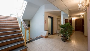 Vestíbulo de hotel con escaleras, una planta en maceta y un candelabro.