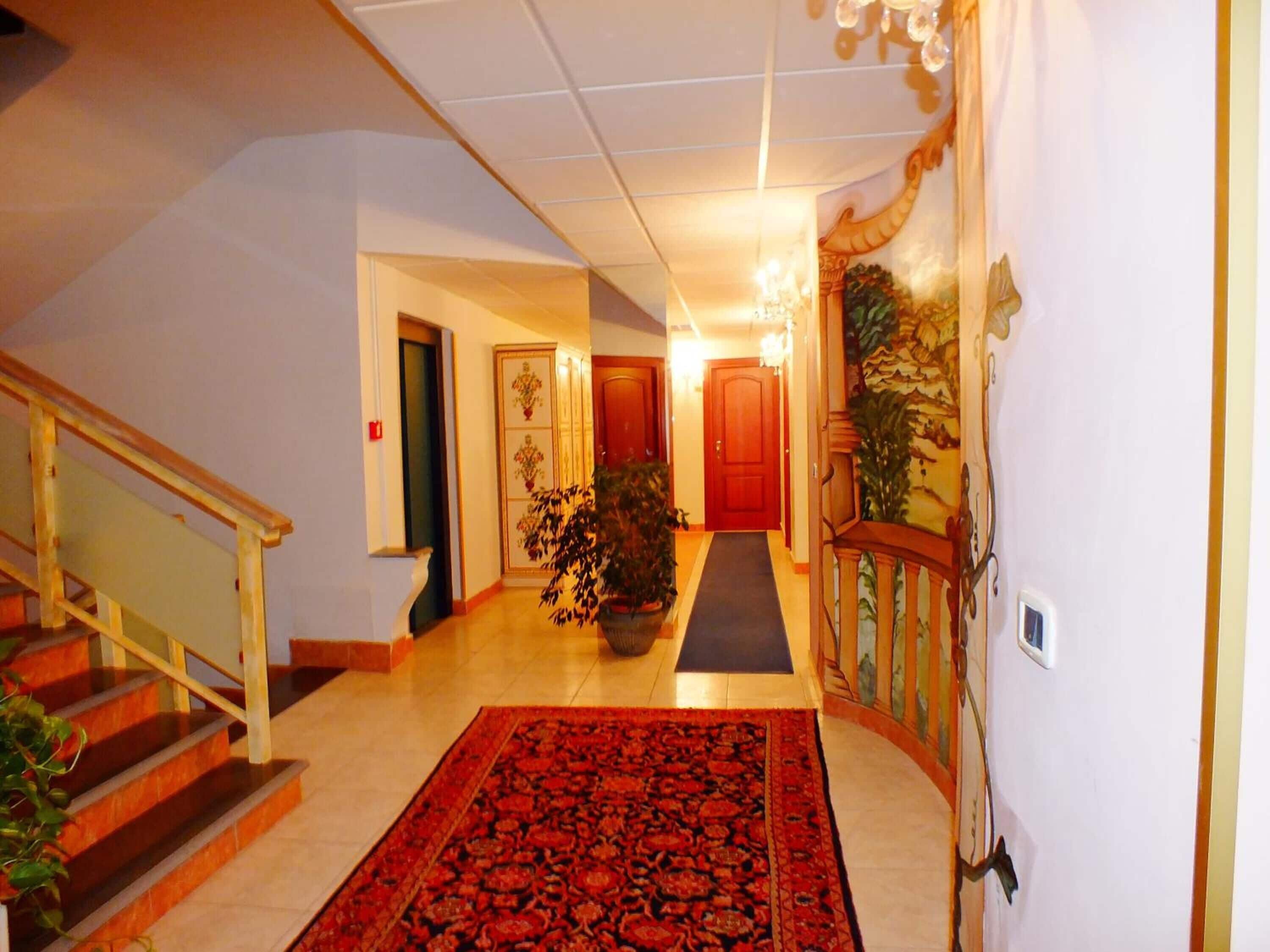 A hallway with a red carpet, wooden staircase, and a door at the end.