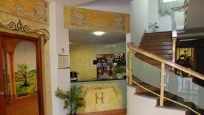 Un vestíbulo de hotel con mostrador de recepción, una escalera y un mural en la pared.