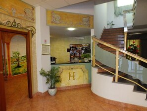 Eine Hotlellobby mit einer Rezeption, einer Treppe und einem Wandgemälde.