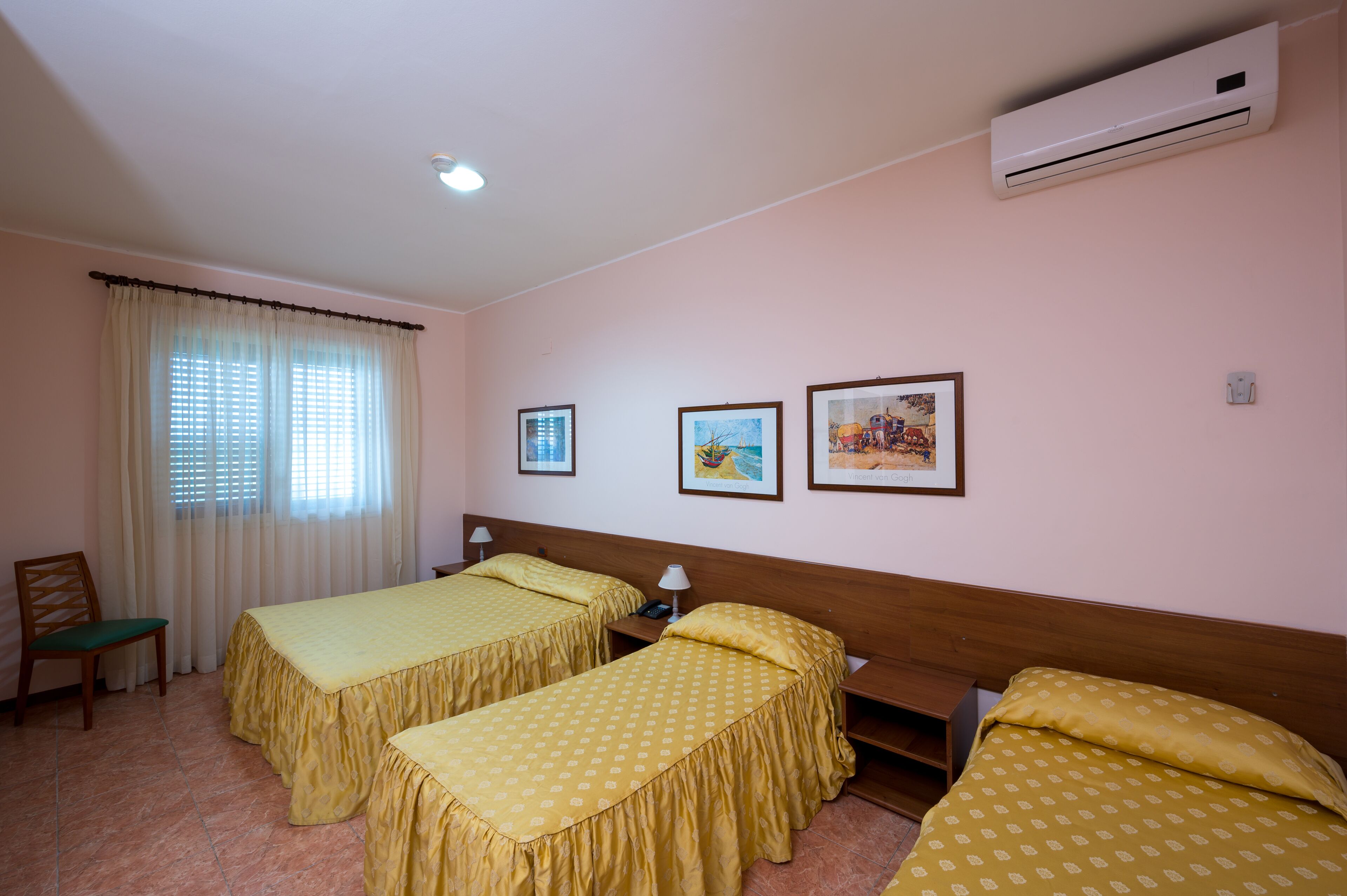 A hotel room with two single beds, a chair, a desk, and a window with curtains.