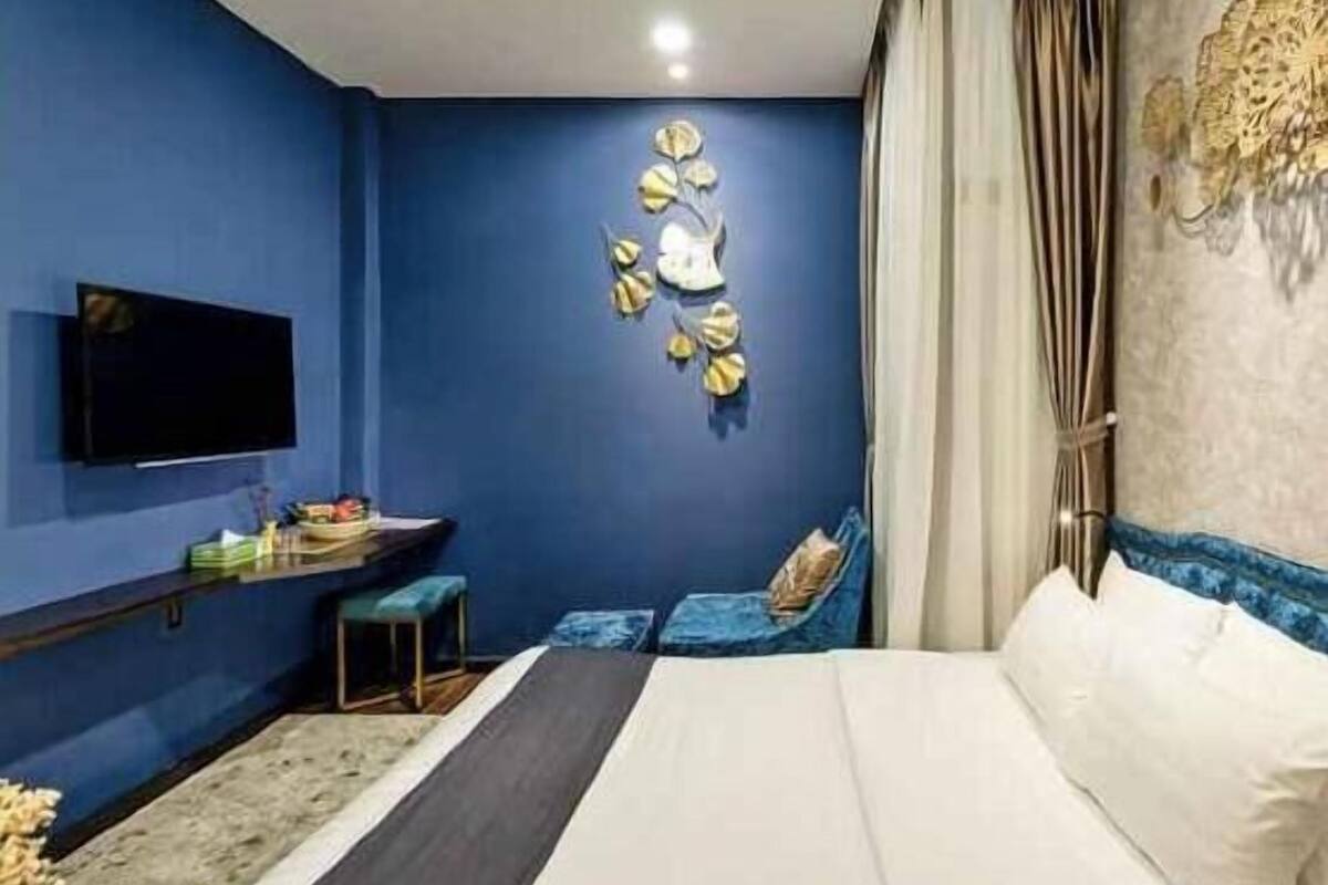 A bedroom with a bed, a TV, a decorative wall piece, and a small seating area.