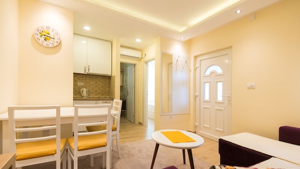 Un soggiorno moderno con zona pranzo, una cucina sullo sfondo e una porta che conduce in un'altra stanza.
