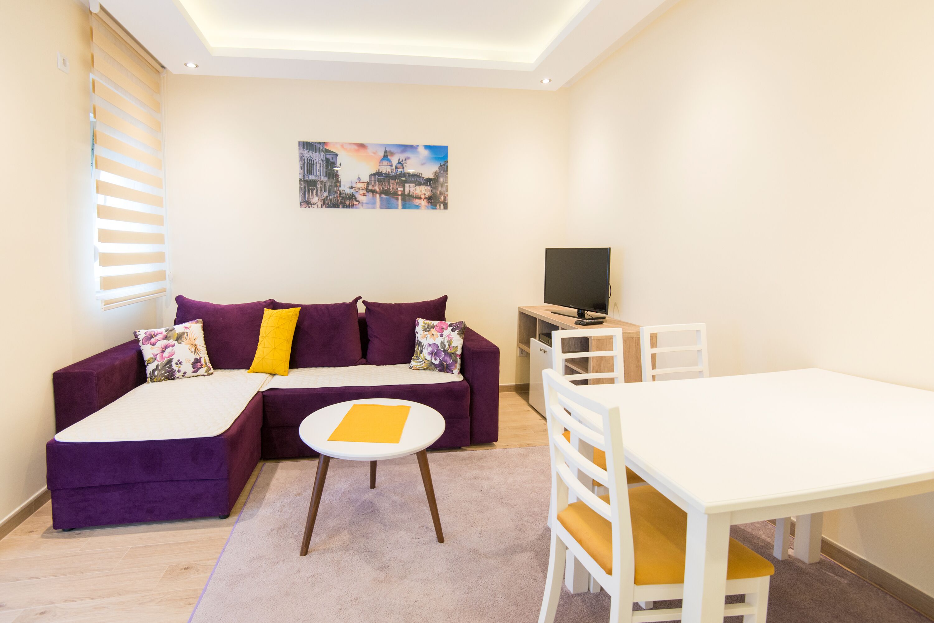 A modern living room with a purple sectional sofa, a white table, and a TV.