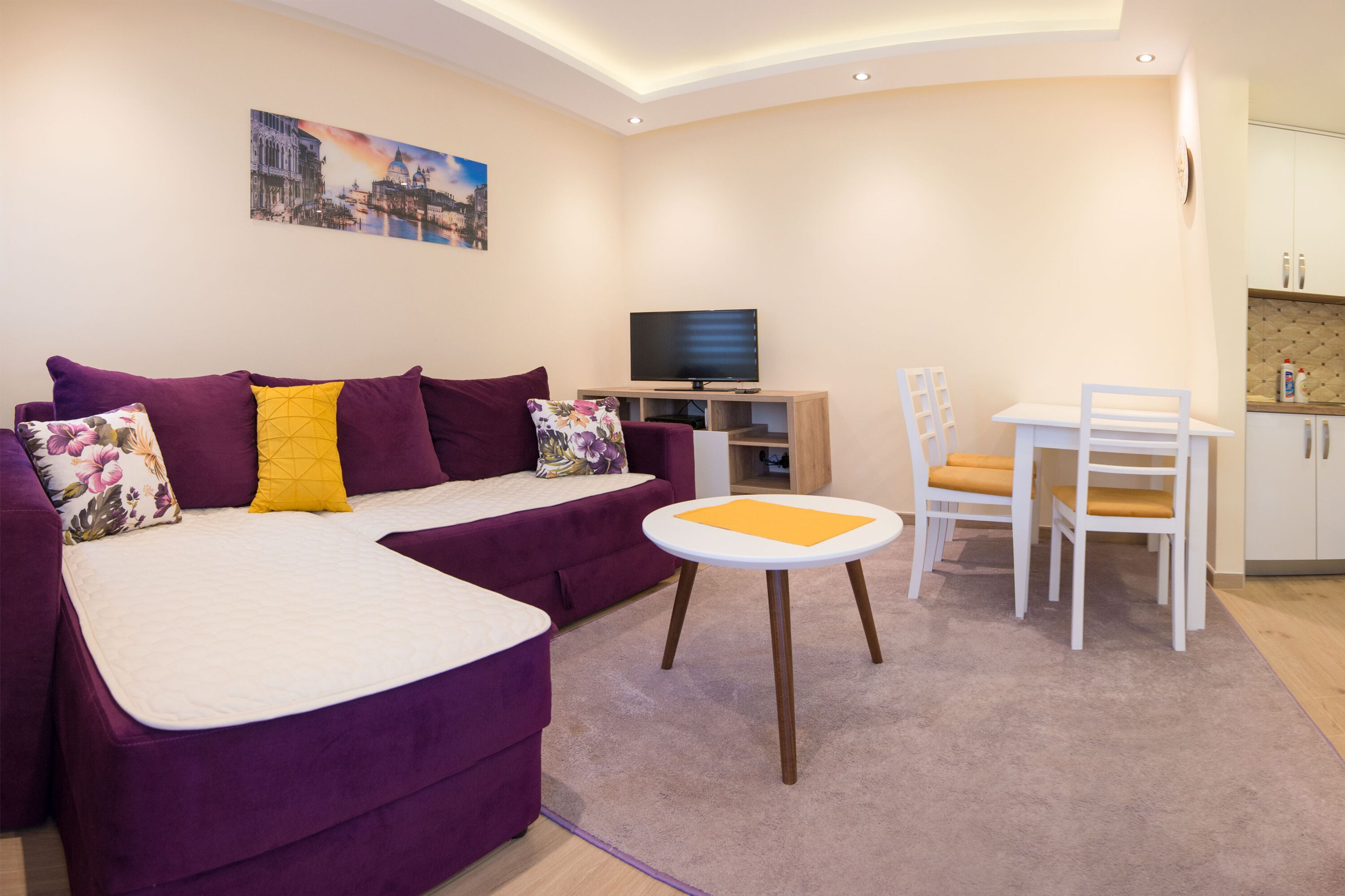 A modern living room with a purple sofa, a small white table, and a TV.