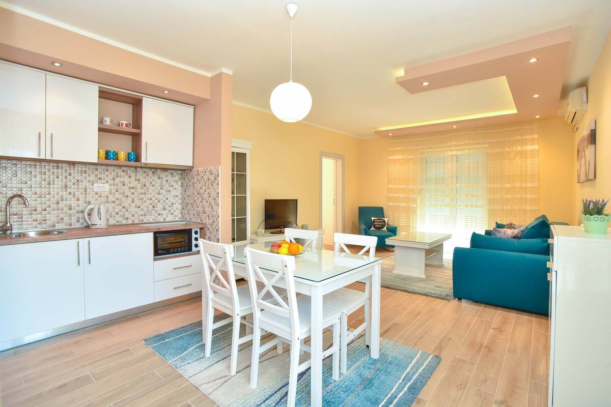 A modern kitchen with white cabinets, a dining table with chairs, and a blue rug.