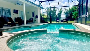 A swimming pool with a hot tub in the center, surrounded by lounge chairs and a glass-enclosed patio.