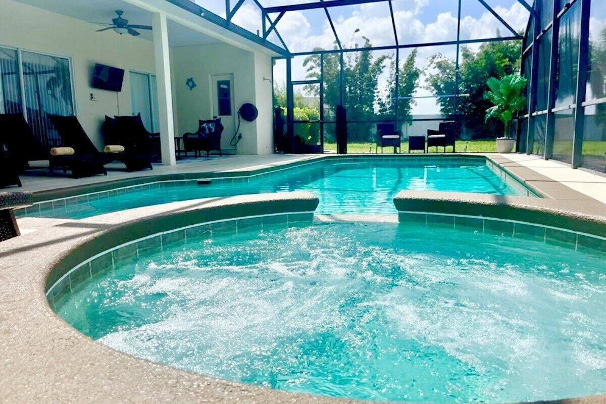 A swimming pool with a hot tub in the center, surrounded by lounge chairs and a glass-enclosed patio.