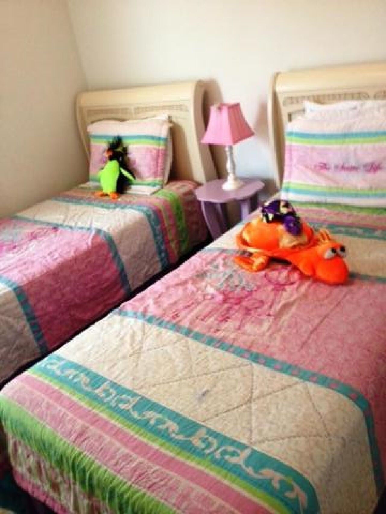 Een tweepersoonskamer met twee bedden, elk met een kleurrijke sprei en kussens. Er staat een klein tafeltje met een lamp tussen de bedden.