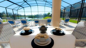 A conservatory with a table set for a meal, overlooking a lake and golf course. - Orlando Renters (Davenport)