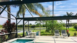 A covered pool area with a view of a golf course, surrounded by palm trees and a grassy landscape.