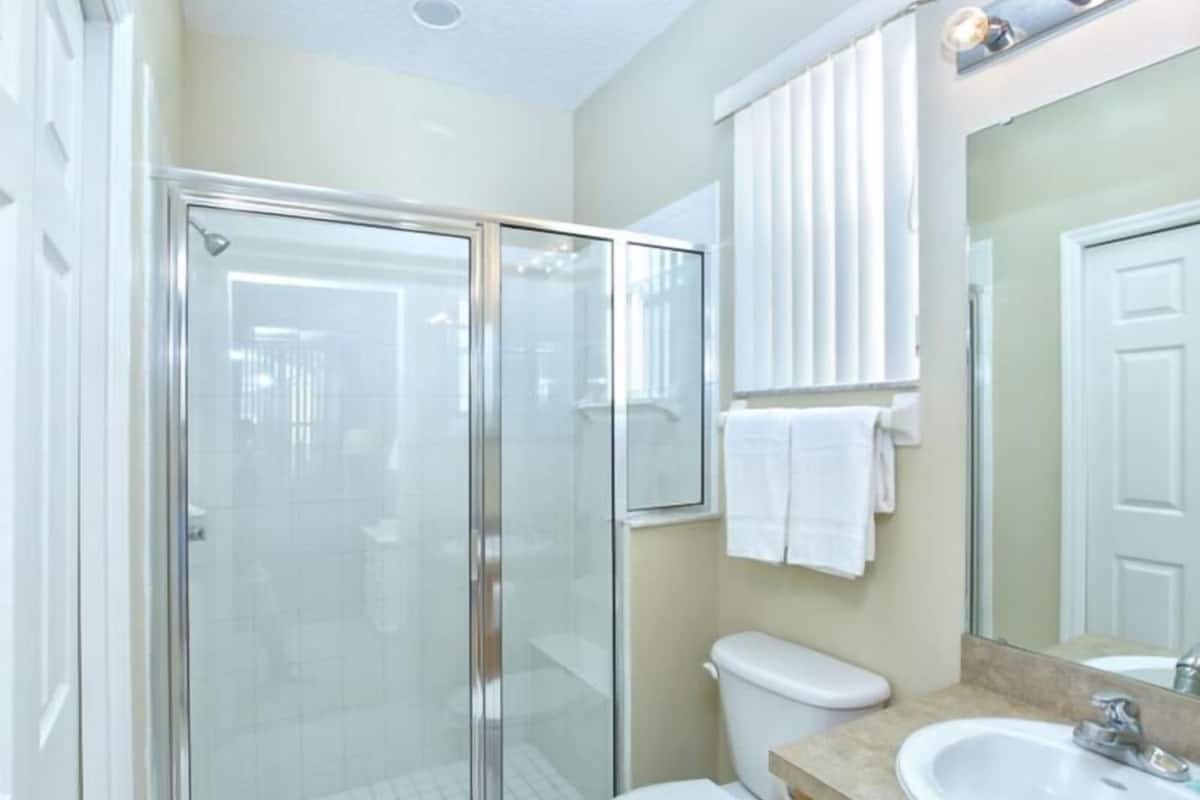 A modern bathroom with a glass-enclosed shower, a toilet, a sink, and a mirror.