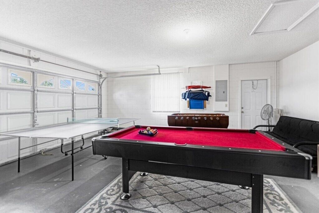 Une table de billard dans une pièce dotée d’une porte de garage, d’un ventilateur et d’un canapé.