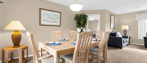 A dining area with a wooden table set for six, surrounded by chairs, a lamp, and framed artwork on the walls.