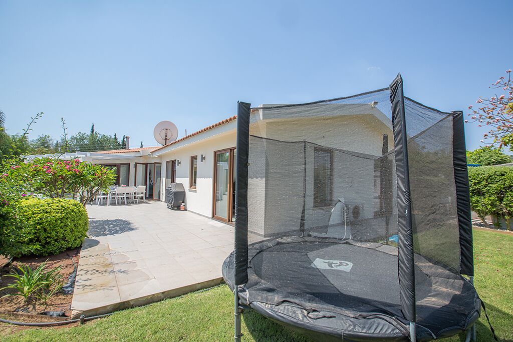 Een achtertuin met een trampoline, een patio en een huis met een schotelantenne.