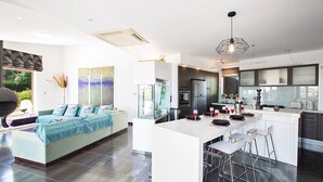Una cocina moderna con una isla central, taburetes de bar y un comedor con sofá.