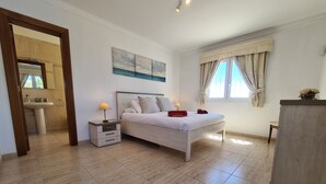 A bedroom with a bed, bedside tables, a window with curtains, a painting on the wall, and a view of the bathroom. - Luxury 3-Bedroom Villa with Private Pool in Los Mojones, Puerto del Carmen (VV) (Puerto del Carmen)