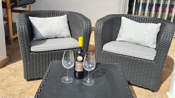 A wicker sofa with cushions, a square table, and two wine glasses with a bottle of wine on it. - Luxury 3-Bedroom Villa with Private Pool in Los Mojones, Puerto del Carmen (VV) (Puerto del Carmen)
