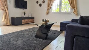 A modern living room with a flat-screen TV, a glass coffee table, a dark sofa, and a beige curtain. - Luxury 3-Bedroom Villa with Private Pool in Los Mojones, Puerto del Carmen (VV) (Puerto del Carmen)