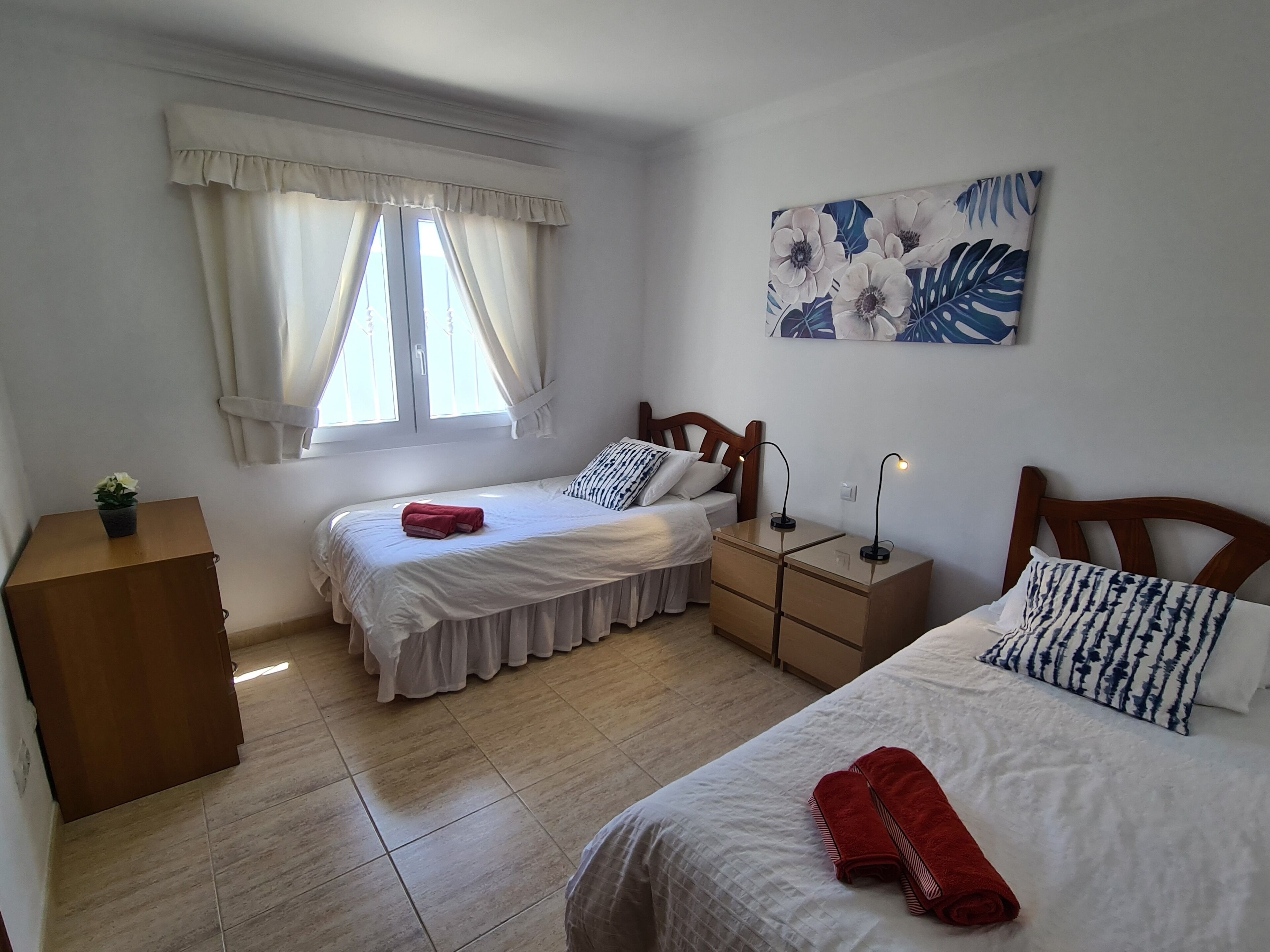 A bedroom with two beds, a nightstand, a dresser, and a window with curtains.