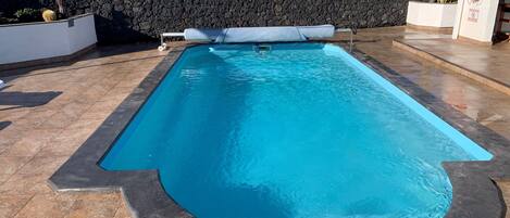 Una piscina rectangular amb mur de pedra i solera emblenada.
