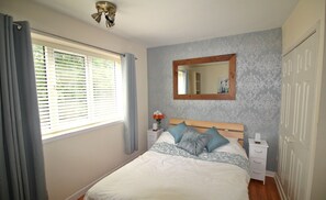 A bedroom with a bed, a bedside table, a nightstand, a mirror, and a window with curtains.