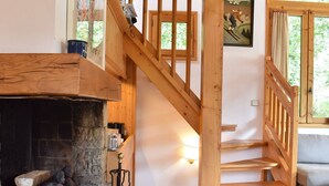 A wooden staircase leading to a second floor, a fireplace with logs, and a window with a view of greenery.