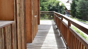 A wooden deck with a railing, leading to a balcony with a view of a mountainous landscape.