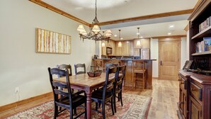 A dining area with a wooden table and chairs, a chandelier, and a kitchen in the background. - Luxurious 2 Bedroom0 Feet From The Slopes! Condo by RedAwning (Avon)