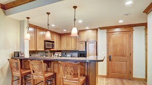 A kitchen with wooden cabinets, a central island with bar stools, and pendant lighting. - Luxurious 2 Bedroom0 Feet From The Slopes! Condo by RedAwning (Avon)