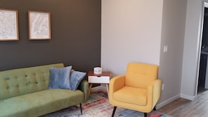A living room with a green sofa, a yellow armchair, and two framed maps labeled 'Paris' and 'New York.' - Awesome new unit available!  Walking distance to great Amherst places and events (Amherst)