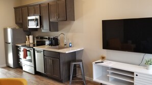 A modern kitchen with dark cabinets, stainless steel appliances, a large flat-screen TV, and a white entertainment unit. - Awesome new unit available!  Walking distance to great Amherst places and events (Amherst)