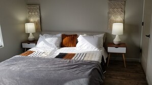 A neatly made bed with a gray blanket, two bedside tables with lamps, and a wall-mounted macrame piece. - Awesome new unit available!  Walking distance to great Amherst places and events (Amherst)