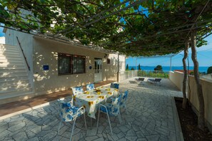Una veranda riparata all'aperto con tavolo e sedie, una scala e vista sul mare.