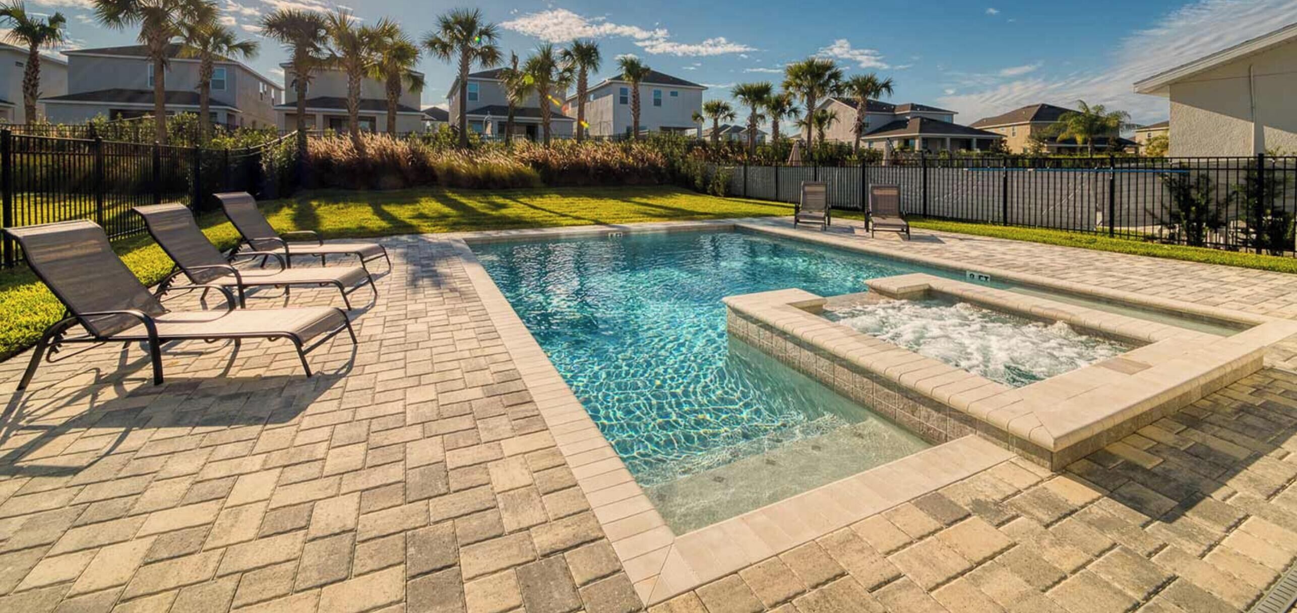 A swimming pool with lounge chairs, a hot tub, and a brick patio.