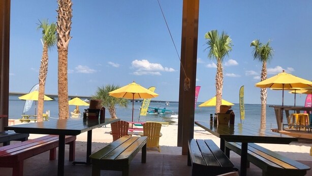 An outdoor seating area with tables and benches, palm trees, and umbrellas. - PERFECT VIEW!!! Waterfront, Marina and 2 Pools! (Fort Walton Beach)